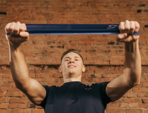 Man performing workout with resistance band against a brick wall backdrop.